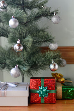 Colorful wrapped presents placed under Christmas tree decorated with silver baubles on wooden table