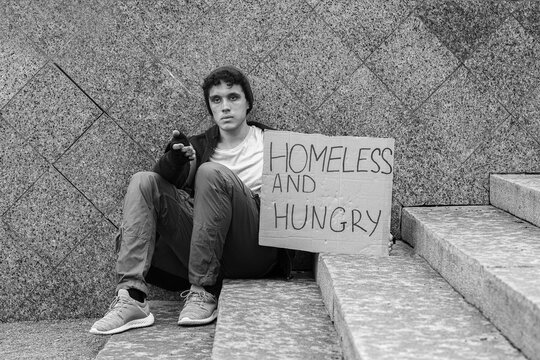 Homelessness and poverty crisis, young man begging for help with a sign on city steps, social inequality and economic hardship in urban environment