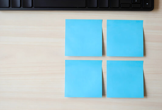 Productivity and task management, four blank blue sticky notes on a wooden office desk with a computer keyboard for planning and project organization