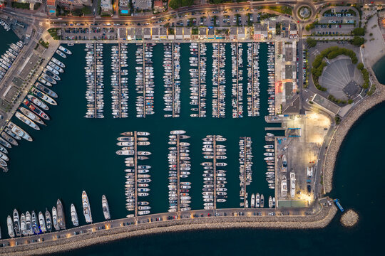 Aerial view of the marina in Antibes with rows of docked yachts and sailboats, illuminated by evening lights along the pier in Antibes, Provence-Alpes-Cote d'Azur, France.