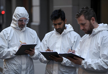 Naklejka na ściany i meble Public health inspection and safety investigation, diverse team of experts in protective hazmat suits writing on clipboards during emergency response