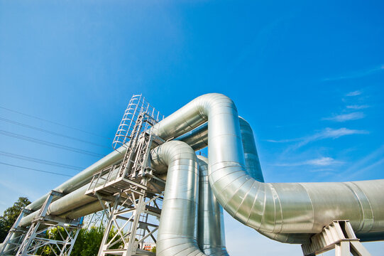 The photo shows a curved pipeline and a power transmission tower against a blue sky