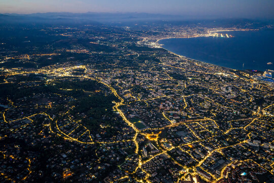 Aerial view of the illuminated city of Antibes at night, featuring glowing street lights, coastal roads, and the Mediterranean coastline in Antibes, Provence-Alpes-Cote d'Azur, France.