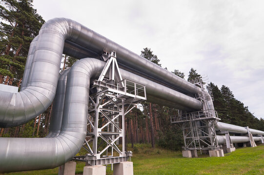The photo shows a pipeline against the backdrop of a gray sky and forest