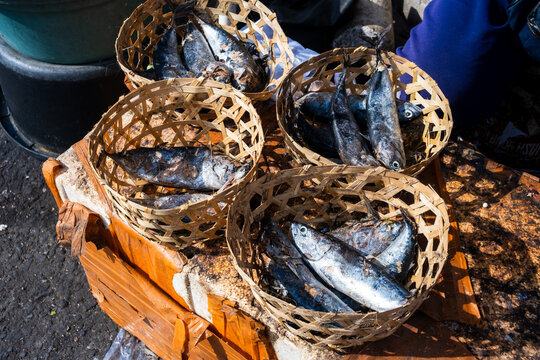 Processed fish (ikan cue) packed in woven bamboo baskets displayed at a traditional market stall.
