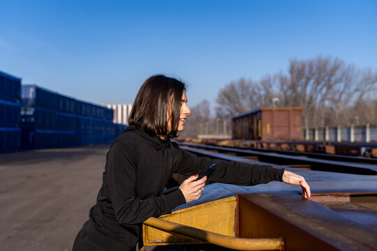 Woman holding smartphone and looking away in a shipping container terminal