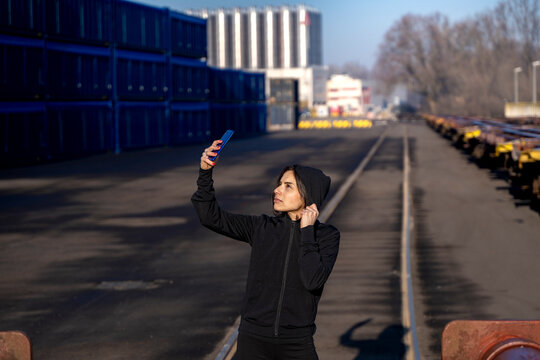 Woman taking a selfie with her smartphone in an industrial shipping container yard