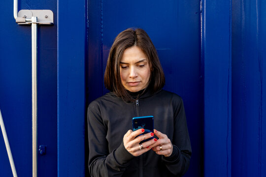 Woman using smartphone for communication and connection against blue wall