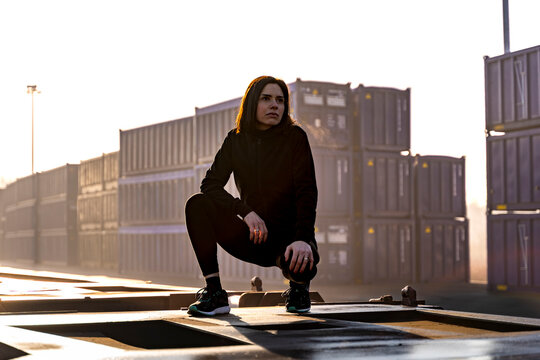 Woman performing squats in sportswear, showing determination in a shipping container terminal at sunshine