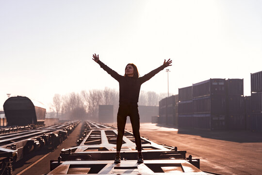 Woman standing on empty freight train car with arms raised at cargo terminal celebrating freedom