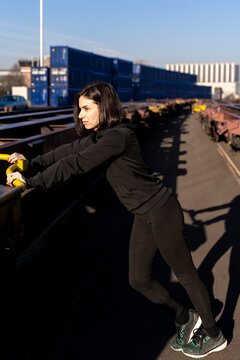 Woman stretching arms and legs on a train car in an industrial setting preparing for a workout