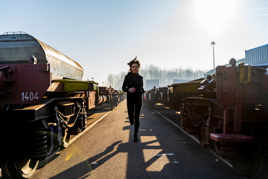 Woman running outdoors in industrial area between train wagons on sunny morning