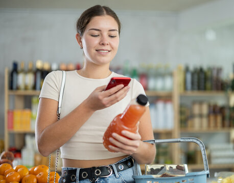 Woman in store scans QR code on grapefruit juice bottle. With help of mobile app, buyer receives information about product. She checks manufacturers data in registry database of national agency