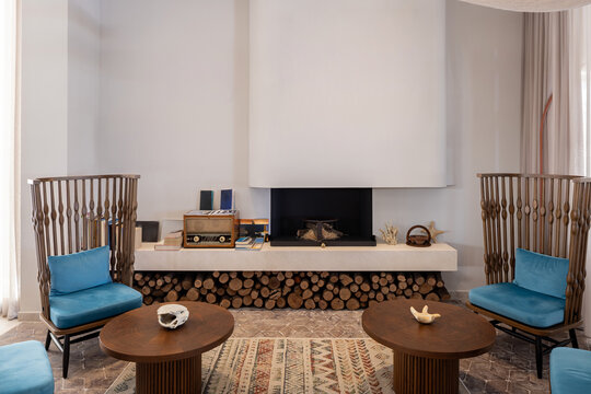 Cozy hotel fireplace lounge with wooden chairs coffee tables and stacked firewood