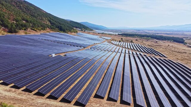 Solar panels cover many rows in a hilly location, reflecting sunlight. This scene highlights the use of renewable energy in open land under a clear sky.