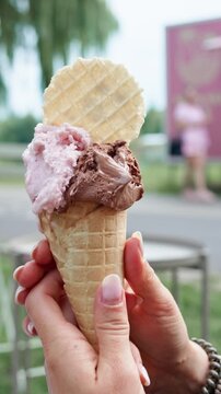 Woman sits in the park holding an ice cream cone and takes a bite while people enjoy the day around her