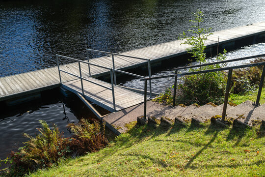 Stone stairs leading to a wooden dock on the calm water of the Caledonian Canal at Fort Augustus in the Highlands of Scotland during a bright day
