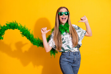 Cheerful young woman in tropical printed shirt with green boa posing against vibrant yellow...