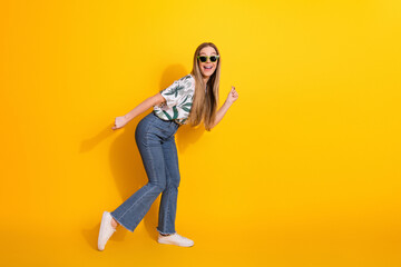 Cheerful young woman in trendy summer attire posing joyfully on a vibrant yellow background