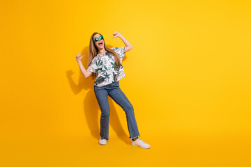 Funny young woman in a vibrant patterned shirt and trendy sunglass striking a playful pose against a bold yellow background © deagreez