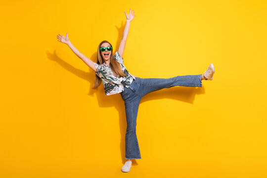 Cheerful young woman in a stylish casual outfit striking a fun pose against a vibrant yellow background