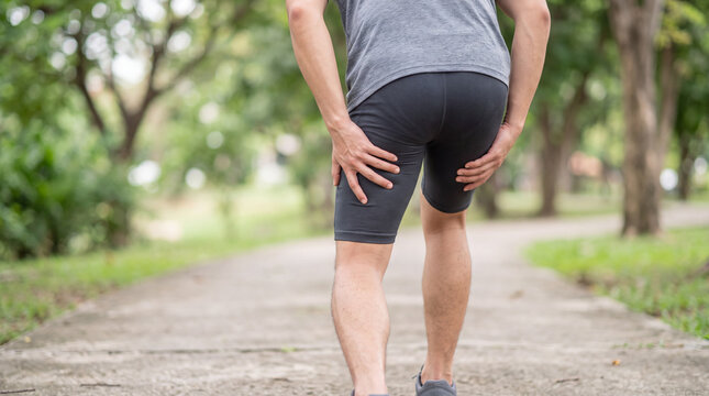 Man holding his painful hamstring while running on an outdoor path