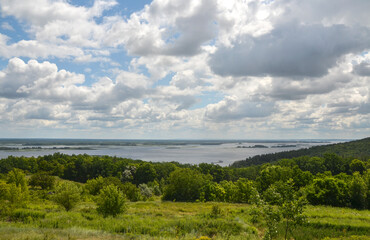 Obraz premium Scenic panoramic view of the wide Dnipro River and green islands from the grassy hills near Vytachiv village in Ukraine, framed by a bright summer sky with clouds