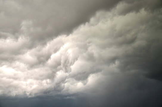 Dramatic dark storm clouds roll across the sky, creating ominous, moody atmosphere that signals heavy rain and turbulent weather. Soft light highlights the textured, layered cloud formations and depth