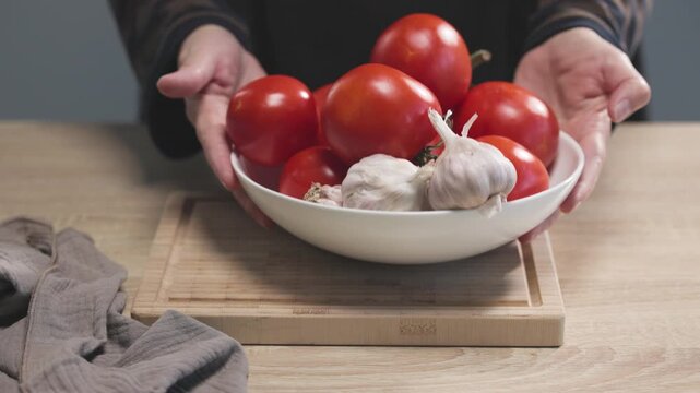 chef places  bowl of fresh tomatoes and garlic on a wooden kitchen table to prepare a healthy meal, food closeup. Ingredients for tomato pasta