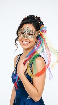 Joyful woman wearing ornate masquerade mask with colorful ribbons and elegant blue dress