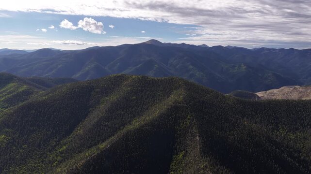 Aerial of forested Sangre de Cristo mountain range and rolling hills under a cloudy morning sky in Carson National Forest near Questa New Mexico