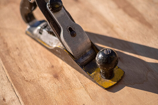 Vintage hand plane with worn yellow paint sits on a wood surface, close up. Useful for woodworking, carpentry, DIY, craft, and home improvement content. Selective focus.