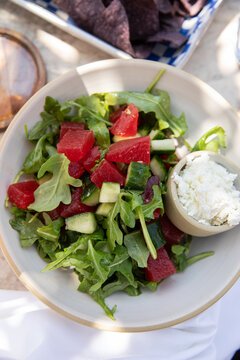 overhead shot of arugula salad with chunks of watermelon and side of feta cheese in an upscale restaurant patio