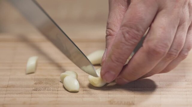 Chef chops fresh garlic cloves on a wooden cutting board while preparing ingredients for a healthy homemade meal, close-up view,  food closeup. Ingredients for tomato pasta