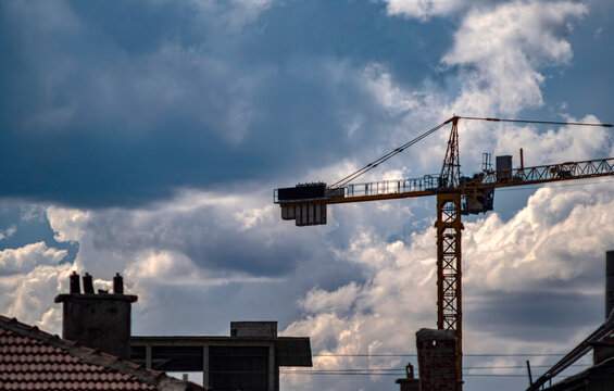 A construction tower crane silhouetted against a cloudy sky above city rooftops. Symbolizing urban development, progress, and architectural growth in an industrial setting.