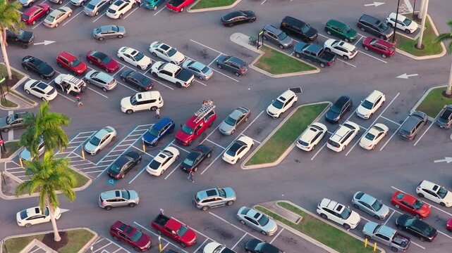 Aerial shot of strip mall with full car parking spaces and continuous vehicle movement, highlighting local business activity, retail sales and transportation flow.