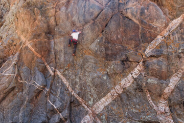 Athletic rock climbers scaling a high vertical crag marked by striking geometric white mineral dykes in an arid canyon landscape. © Valentin
