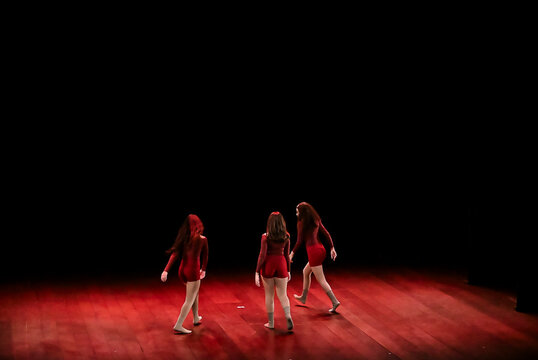 three dancers in red outfits walking on wooden stage, dynamic theater group dance performance, expressive performing arts concept