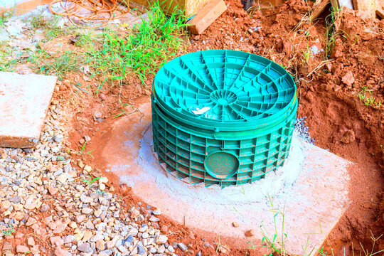 Green septic tank drainage utility structure is placed in ground at construction site among soil gravel.