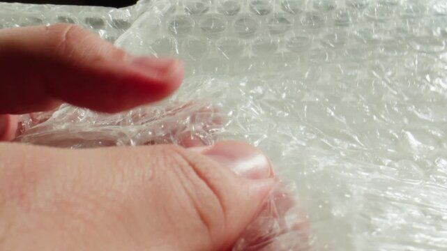 Bubble wrap squeezed in hands, fingers popping plastic film air bubbles extreme close up macro, packaging and stress relief concept
