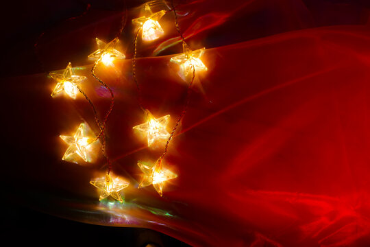 Christmas atmosphere. Glowing Star Shaped Fairy Lights on Red Fabric. decorative LED lights