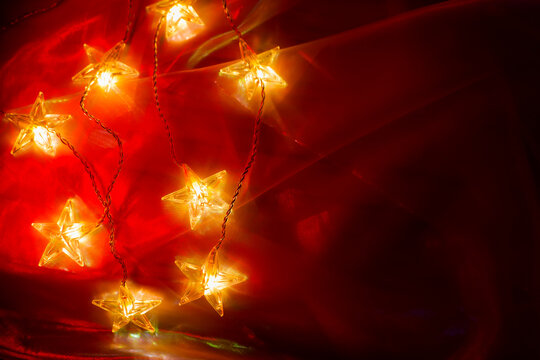 Christmas atmosphere. Garland stars on a red tulle background.Cozy Christmas Decoration.Glowing Star Shaped Fairy Lights on Red Fabric. decorative LED lights