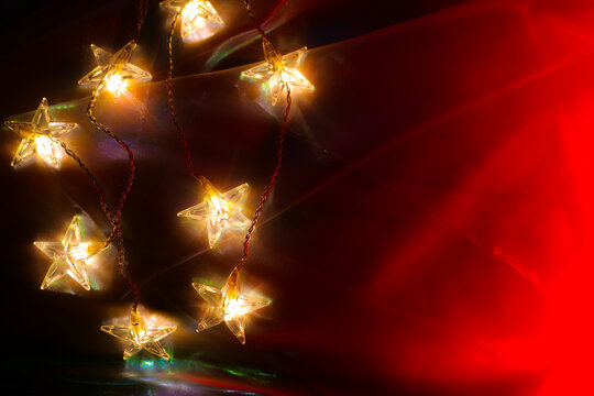 Garland stars on a red tulle background.Cozy Christmas Decoration.Glowing Star Shaped Fairy Lights on Red Fabric. decorative LED lights