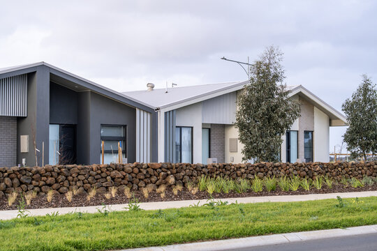 Modern single-story residential townhouses behind a stacked dry-stone retaining wall,&nbsp;and nature strip in a new suburban housing estate in an outer suburb of Melbourne, Victoria, Australia.  