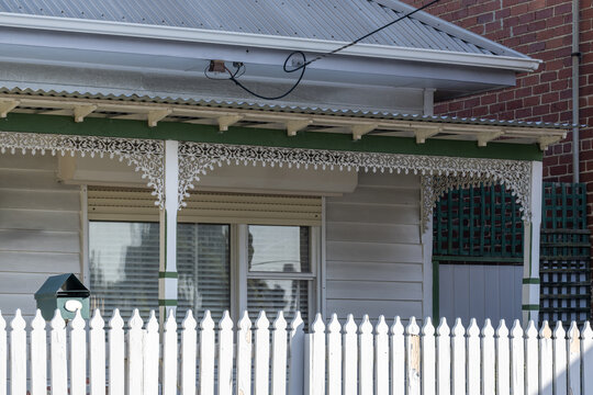 A traditional Australian weatherboard cottage featuring decorative iron lacework trim along the verandah, a white picket fence, a corrugated iron roof. Nostalgic charm in Melbourne, Australia