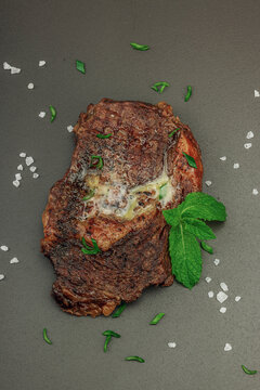 Grilled ribeye steak with melted butter and herbs on dark background, high protein meal concept