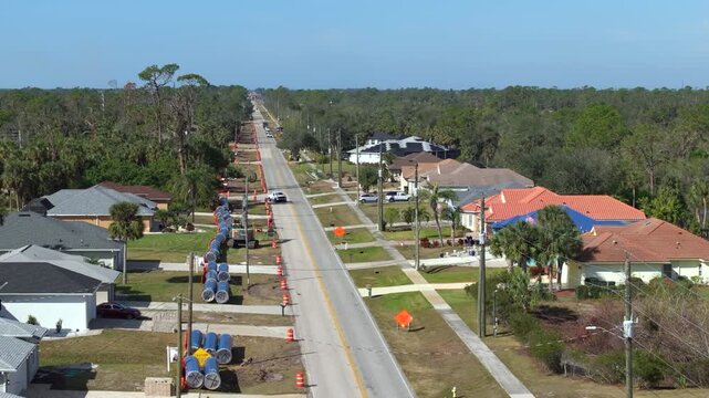 Florida neighborhood street under repair, with one lane closed by cones and temporary lights while vehicles navigate past roadwork equipment.