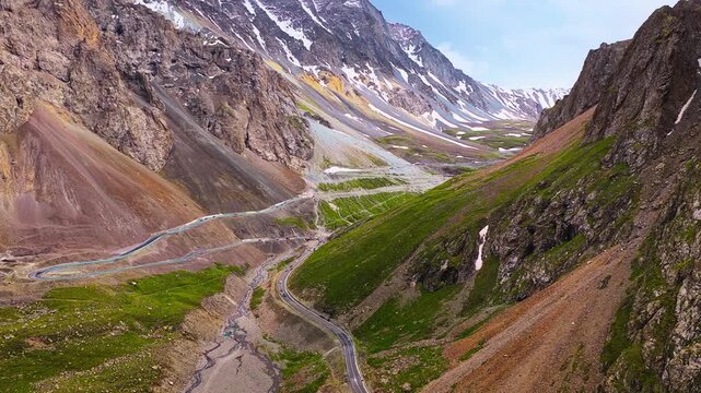 Winding mountain road snakes through a dramatic valley along the Duku Highway in Xinjiang under clear blue daytime skies.