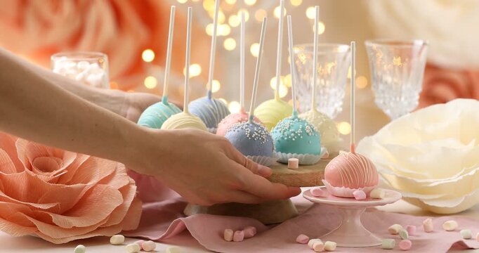 Woman putting stand with tasty cake pops onto white table against blurred lights, closeup