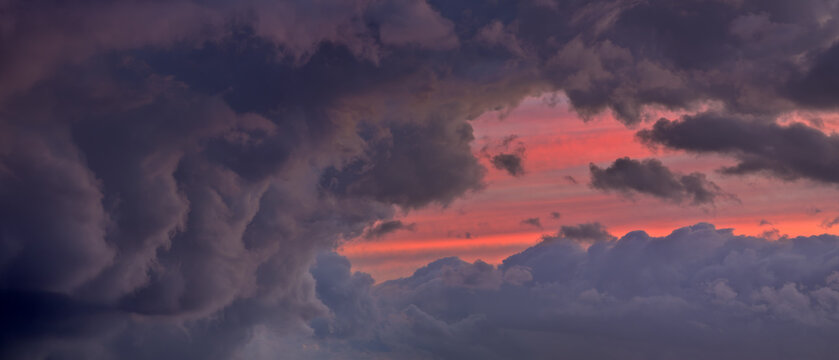 Panoramic view of ominous dark storm clouds parting to reveal a vibrant and striking pink sunset.